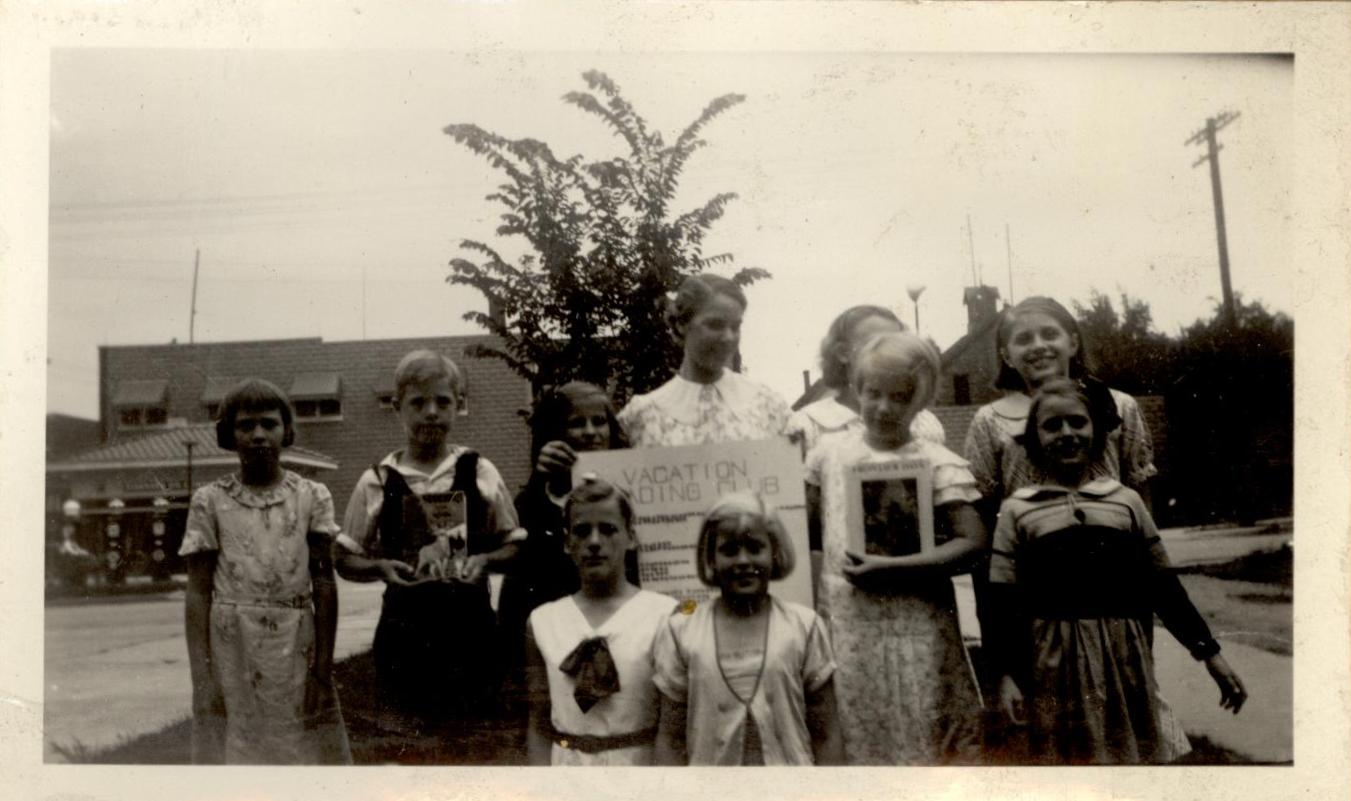 Black and white photo of group of children holding books and a sign for Vacation Reading Club