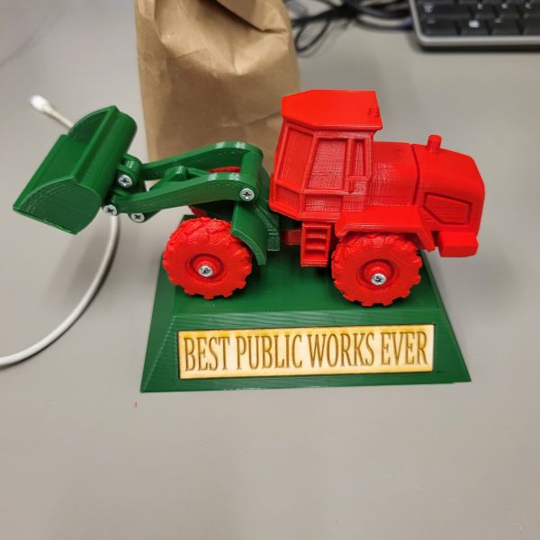Front loader printed separately in parts to create a multicolored print, and then screwed together and glued to a base. The base has a slight recess to accommodate a laser etched wood insert that says BEST PUBLIC WORKS EVER.