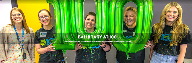 Group of smiling women pose with balloons that spell out the number 100